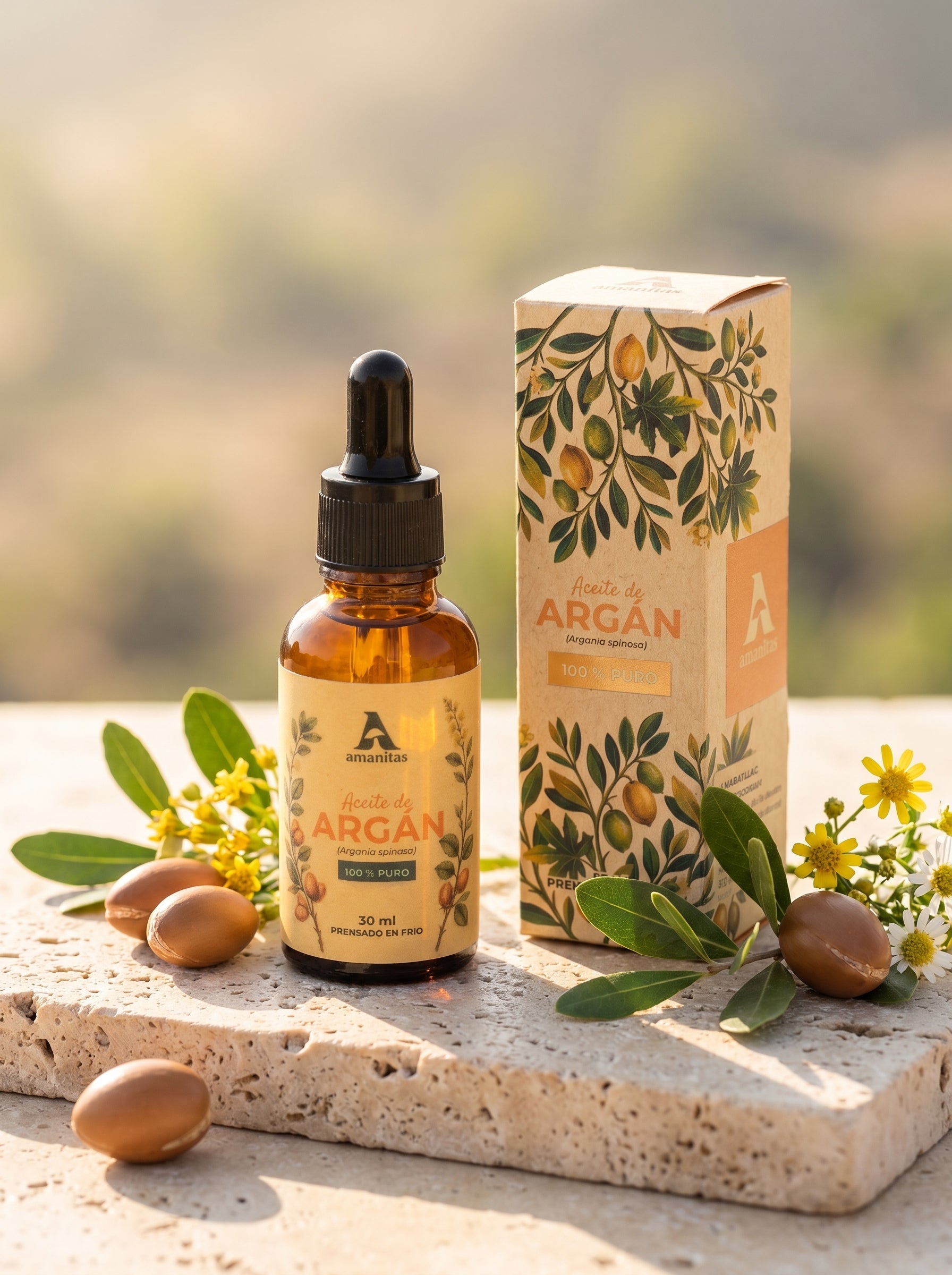 Presentación premium de Aceite de Argán 100% puro Amanitas, mostrando el frasco gotero de 30 ml junto a su empaque exterior decorado con ilustraciones botánicas detalladas. El producto reposa sobre una base de piedra natural, rodeado de semillas de argán reales y flores amarillas, evocando origen natural y pureza.