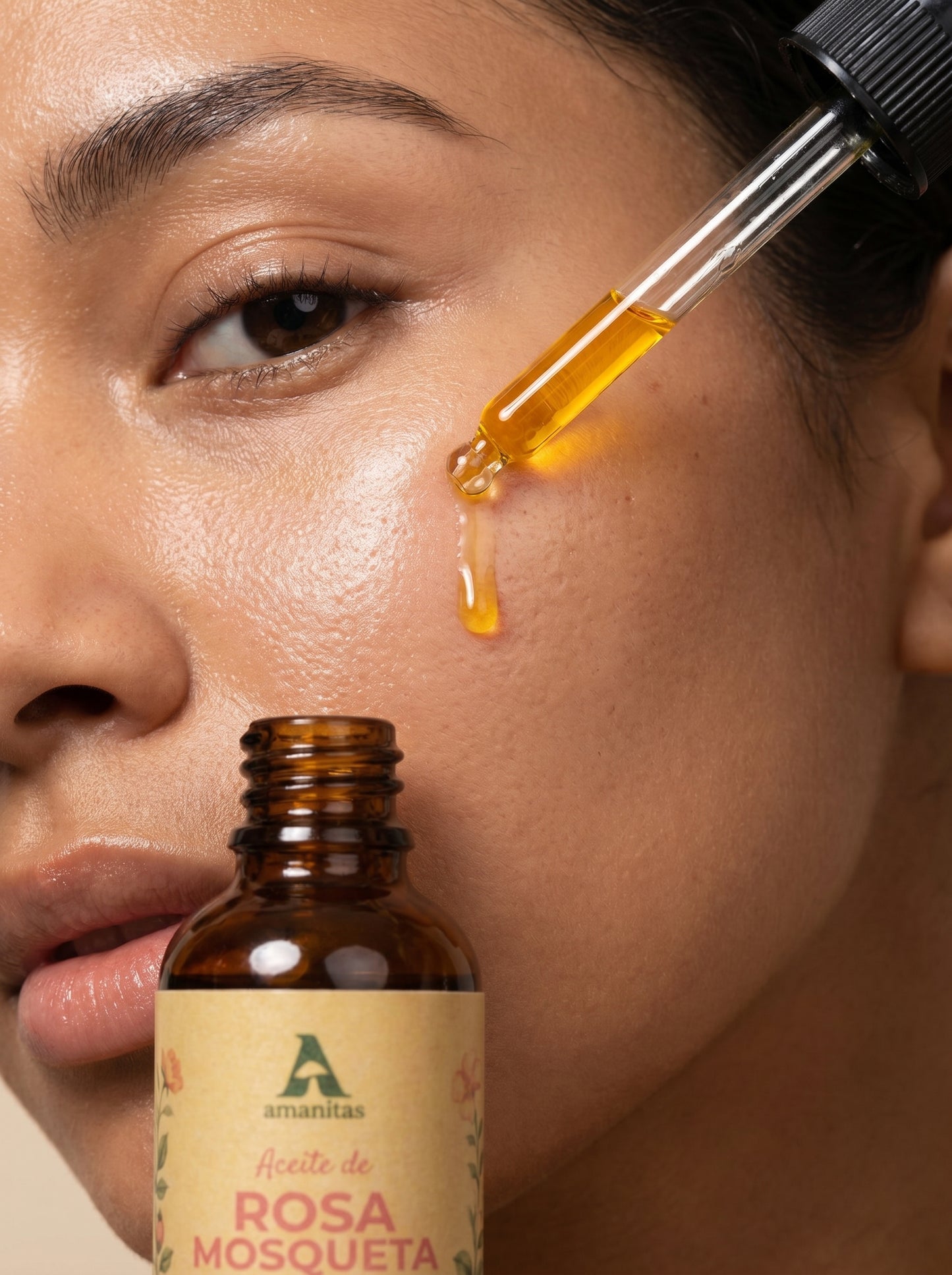Primer plano de una persona aplicando gotas de Aceite de Rosa Mosqueta 100% puro Amanitas directamente sobre la mejilla con un gotero. Se aprecia la textura fluida del aceite y el frasco de vidrio ámbar de 30 ml con etiqueta de diseño botánico, destacando su uso como tratamiento regenerador facial.