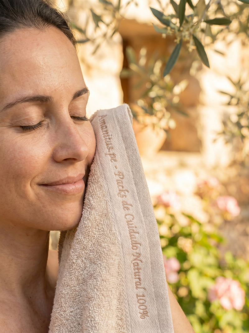 Mujer disfrutando de un momento de serenidad y cuidado personal con una toalla bordada de Amanitas.pe, marca de packs de cuidado natural. La imagen refleja paz, belleza consciente y la experiencia reconfortante de nuestra rutina natural en un entorno lleno de luz.