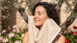 Mujer disfrutando de un momento de serenidad y cuidado personal en un entorno natural al aire libre, sosteniendo una toalla con la marca Amanitas.pe, especialistas en packs de cuidado natural.