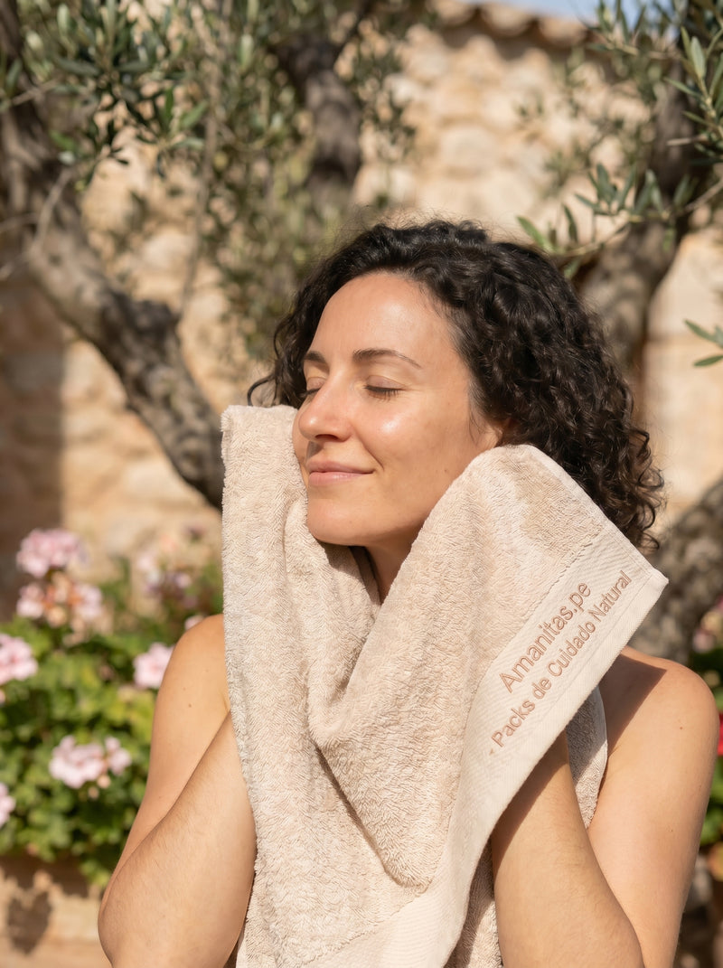 Mujer disfrutando de un momento de autocuidado y serenidad al aire libre, secando suavemente su rostro con una toalla de Amanitas.pe, especialistas en packs de cuidado natural. La imagen refleja paz, belleza consciente y una conexión genuina con los productos de nuestra marca.