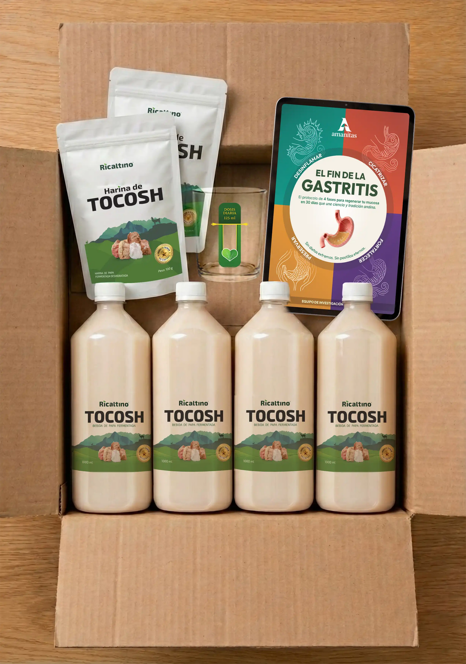 Vista superior de la caja de envío abierta con el pack de Amanitas. Muestra el contenido exacto que recibe el cliente: 4 botellas de bebida de Tocosh Ricaltino, 2 bolsas de harina de Tocosh, un vaso medidor de vidrio y una vista previa del libro digital El Fin de la Gastritis.
