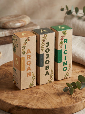 Set de tres aceites naturales de la marca Amanitas: Argán, Jojoba y Ricino. Los empaques de cartón con diseño de ilustraciones botánicas muestran la presentación premium y ecológica de la colección de aceites prensados en frío sobre una superficie de madera.
