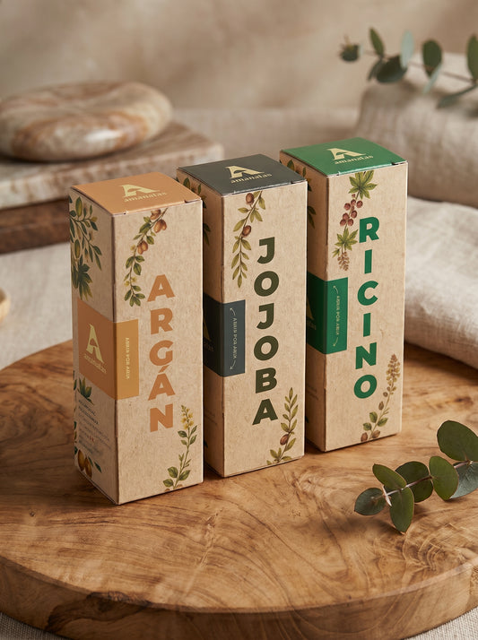 Set de tres aceites naturales de la marca Amanitas: Argán, Jojoba y Ricino. Los empaques de cartón con diseño de ilustraciones botánicas muestran la presentación premium y ecológica de la colección de aceites prensados en frío sobre una superficie de madera.